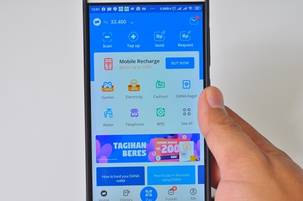 Tangan Seseorang yang Sedang Memegang HP, Ponsel, atau Handphone Android dengan Aplikasi DANA Dompet Digital Indonesia Sebagai Salah Satu Fintech yang Populer di Google PlayStore yang Terbuka di Layarnya