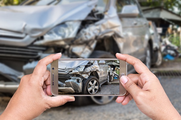 Tangan Wanita Memegang Smartphone dan Ambil Foto Kecelakaan Mobil Sebagai Cara Klaim Asuransi Mobil All Risk